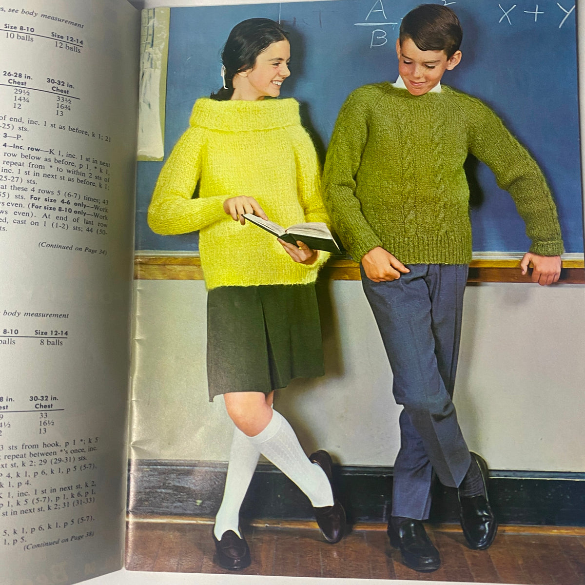 Page from '1964 Vol. 80 Raglans For Boys and Girls Sweater Vest Catalog' displaying two children, a boy and a girl, modeling vibrant knitted pullover sweaters in a classroom setting.