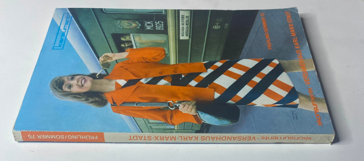 Side view of the 1975 Konsument Summer Catalog, displaying the same cover design with a woman in stylish orange outerwear and a bold striped dress, emphasizing vintage East German fashion.