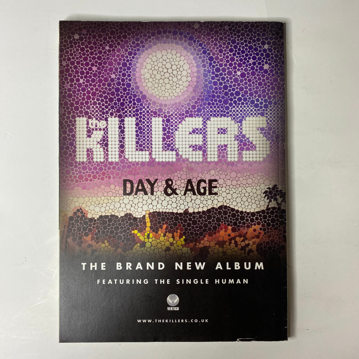Promotional cover for 'Day & Age' album by The Killers, featuring vibrant artwork with desert landscape and celestial elements in a mosaic style.