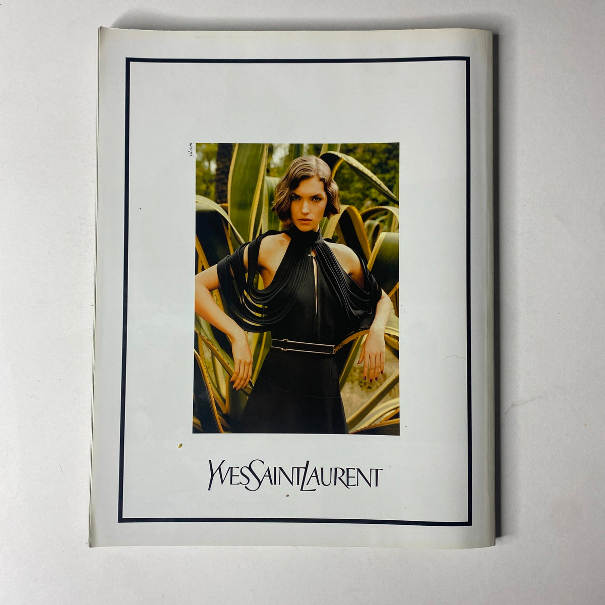 Wes Saint Laurent advertisement displaying a model in an elegant black dress, set against a natural background, from the Vogue Paris Magazine April 2011 No. 916 Gisele Bündchen Cover.