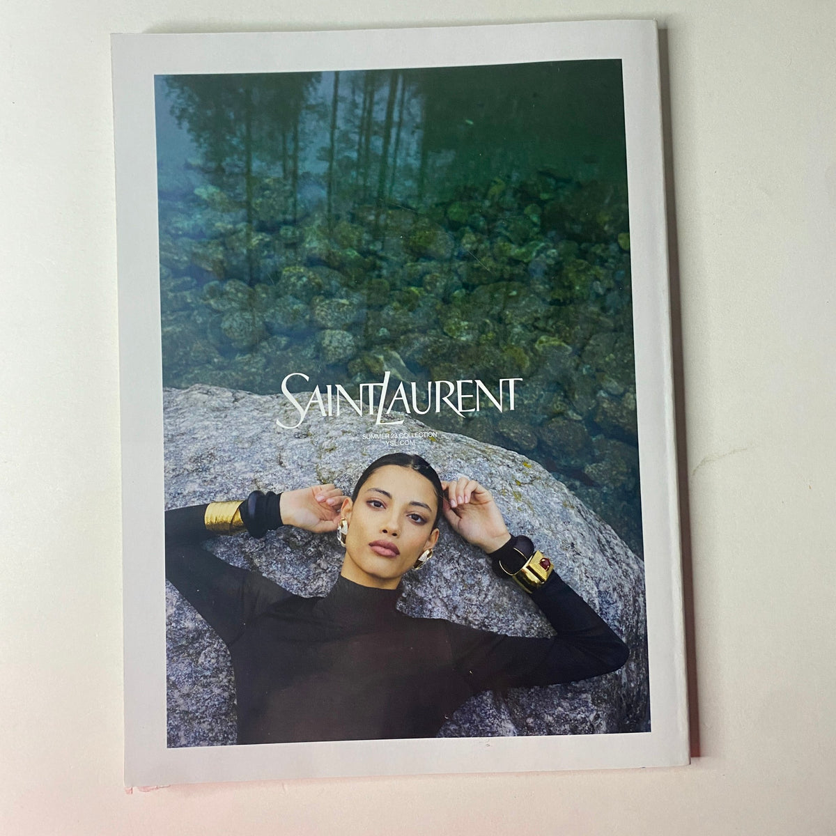 Saint Laurent campaign image featuring a model wearing a black outfit with bold accessories, set against a serene water backdrop, featured in Vogue British Magazine August 2023 with Maya Jama on the cover.