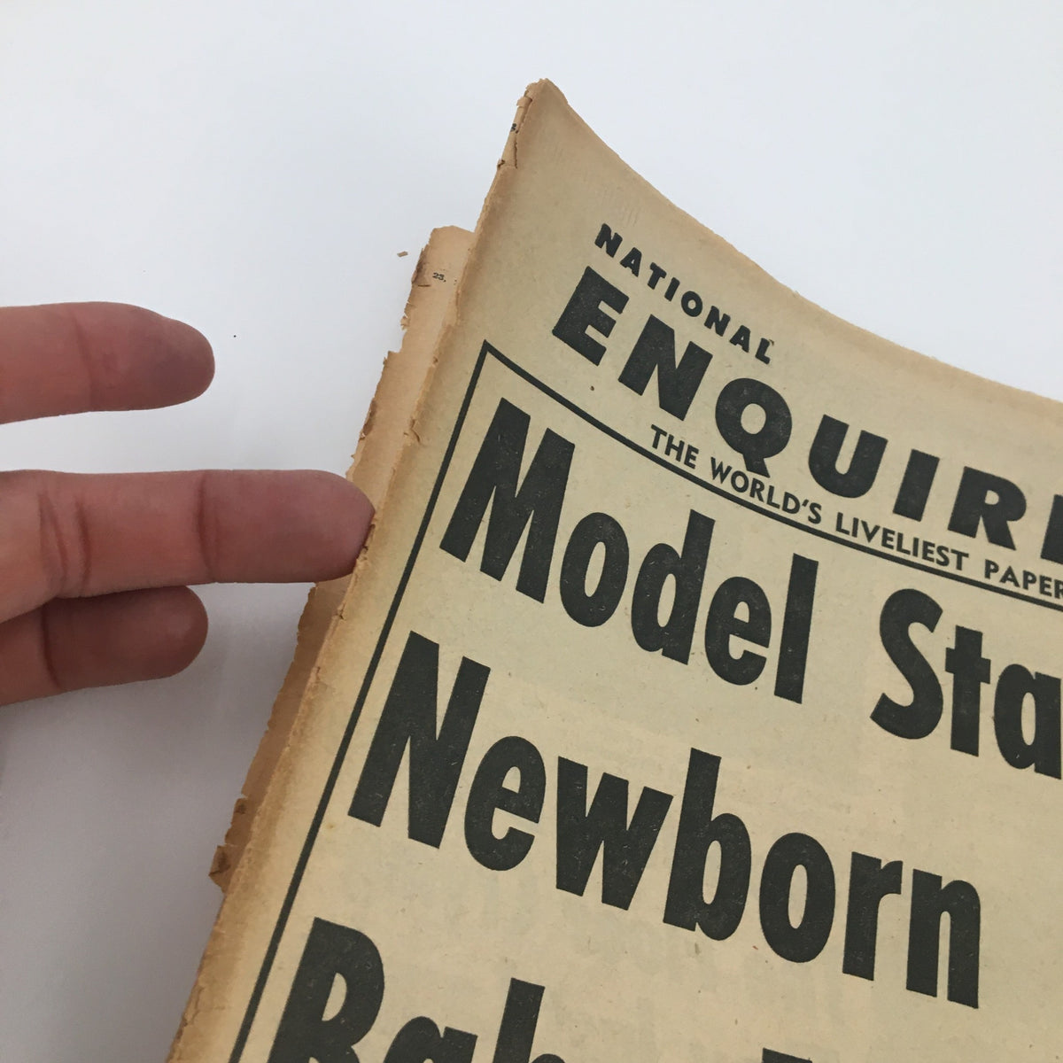 Close-up of the National Enquirer Newspaper from September 23, 1962, highlighting the headline 'Model Stabs Her Newborn Baby' with visible wear and age.