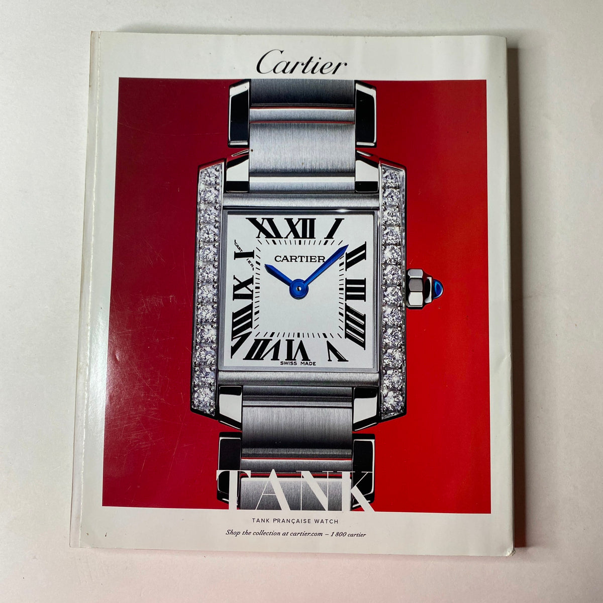 Cover of the Cartier Tank Pancake Watch advertisement featuring a luxurious silver watch against a vibrant red background. This promotional image showcases the elegance and design of the Tank watch, perfect for watch enthusiasts.