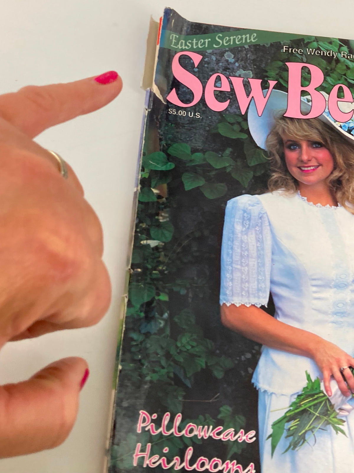 Close-up of the Sew Beautiful Magazine Easter 1994 cover, showing wear on the edges and a finger pointing at the title. The magazine features polka dot shadow embroidery and is part of vintage crafting history.