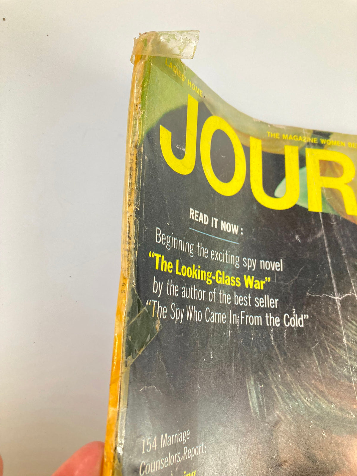 Side view of the VTG Ladies' Home Journal Magazine April 1965, showcasing wear and tear typical for its age, including a label and text about upcoming articles including 'The Looking-Glass War'.