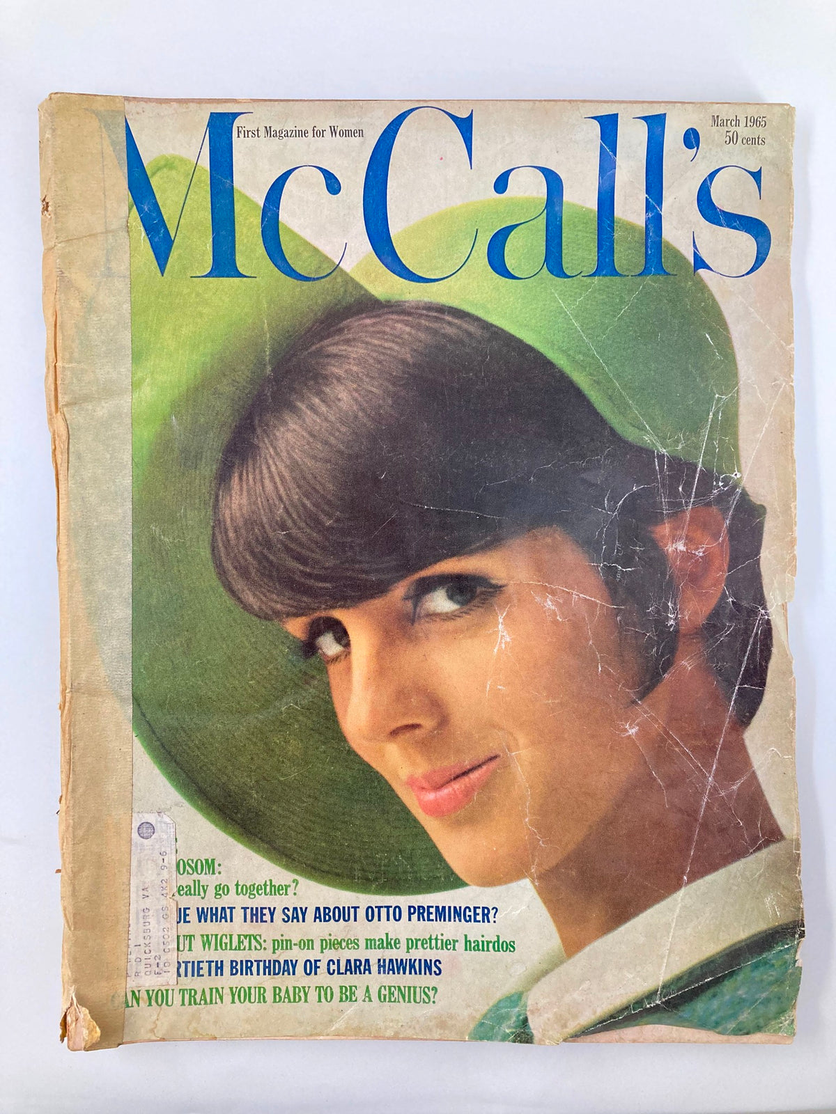 Vintage McCall's Magazine March 1965 cover featuring a woman with a stylish green hat, photographed by O. Storch, showing wear and an address label.
