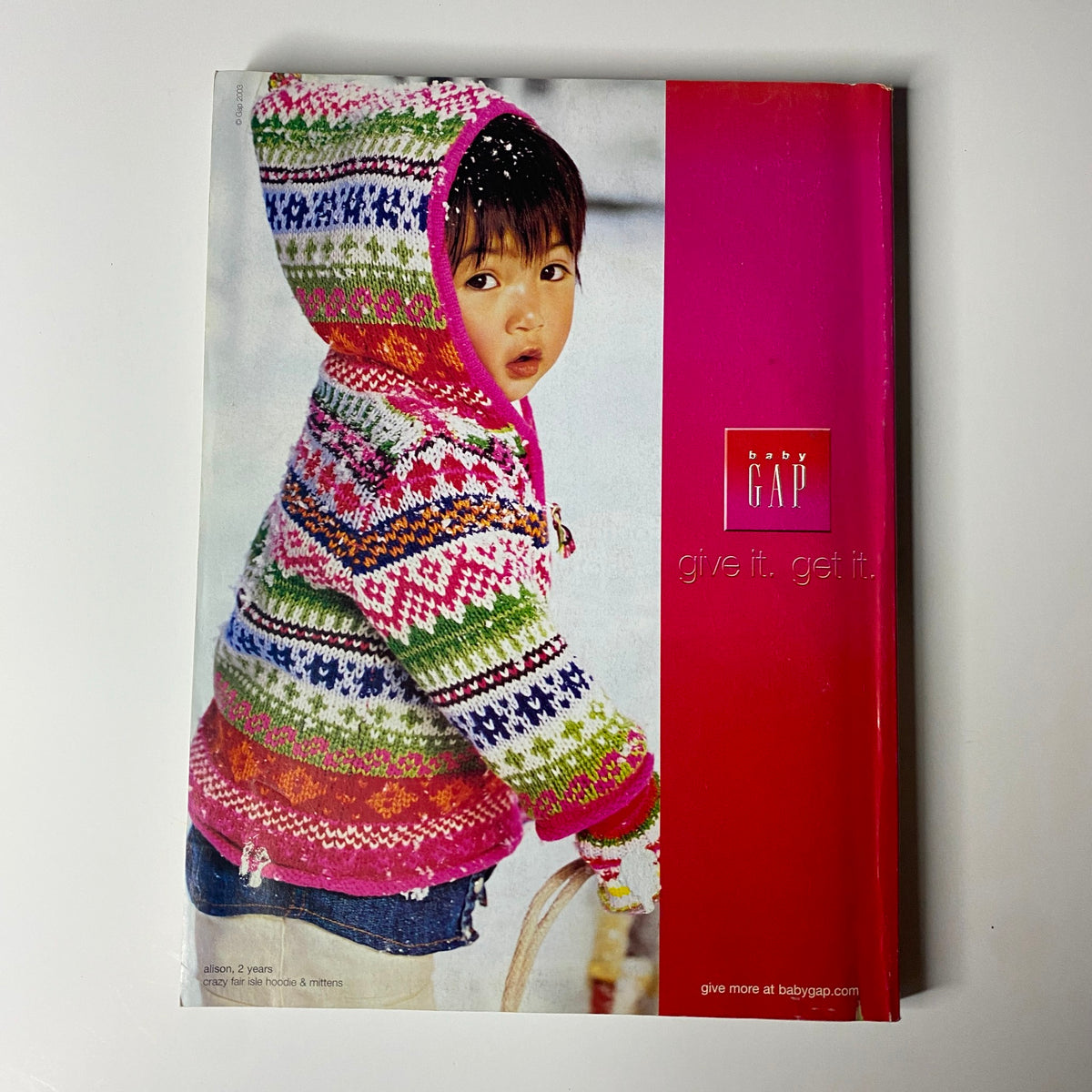 Vogue Magazine December 2003 showcasing a child in a playful outdoor setting, wearing a colorful knitted hoodie from Gap, surrounded by snow.