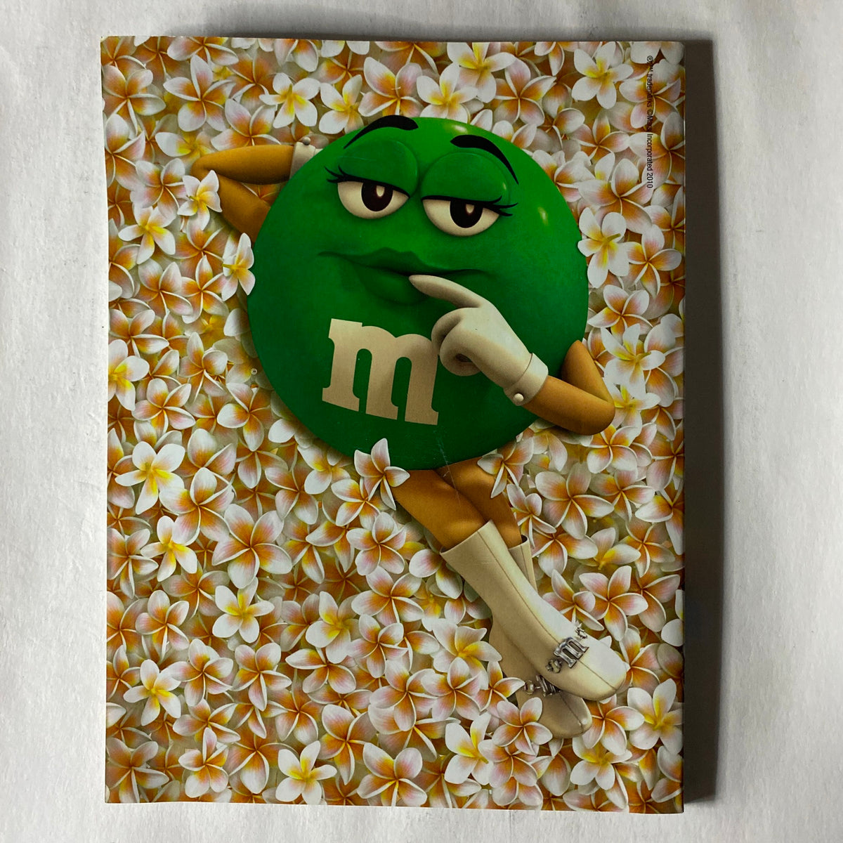 M&M's character lounging amidst a backdrop of tropical flowers, featured in a playful advertisement.