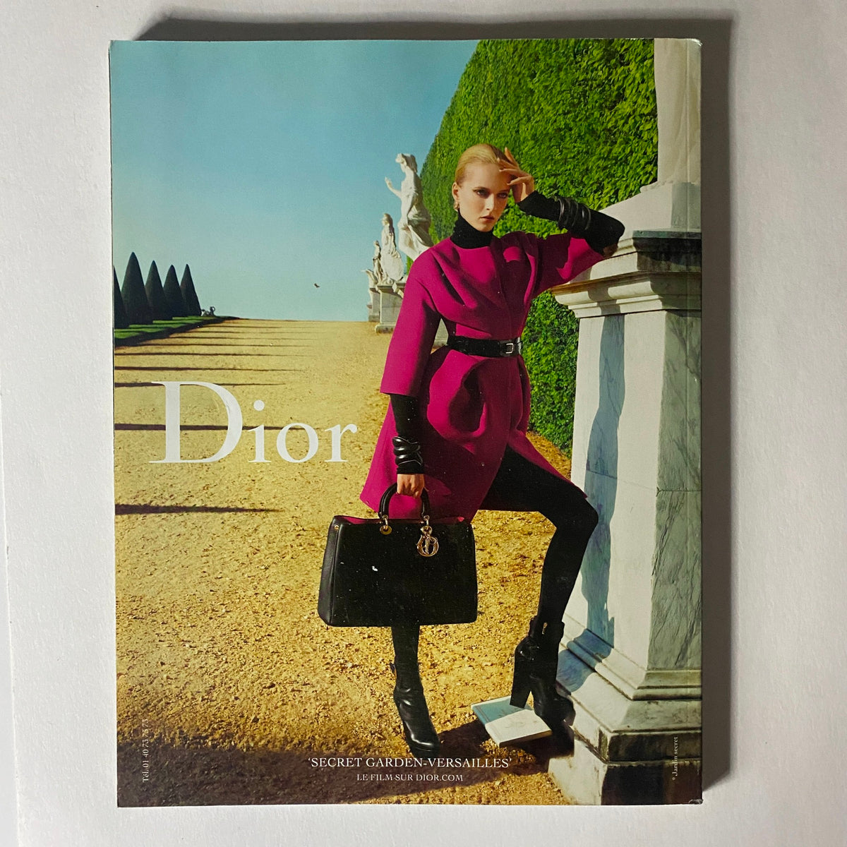 Fashion advertisement in Numéro Magazine August 2012 featuring a model in a pink Dior coat, set against an elegant garden backdrop.
