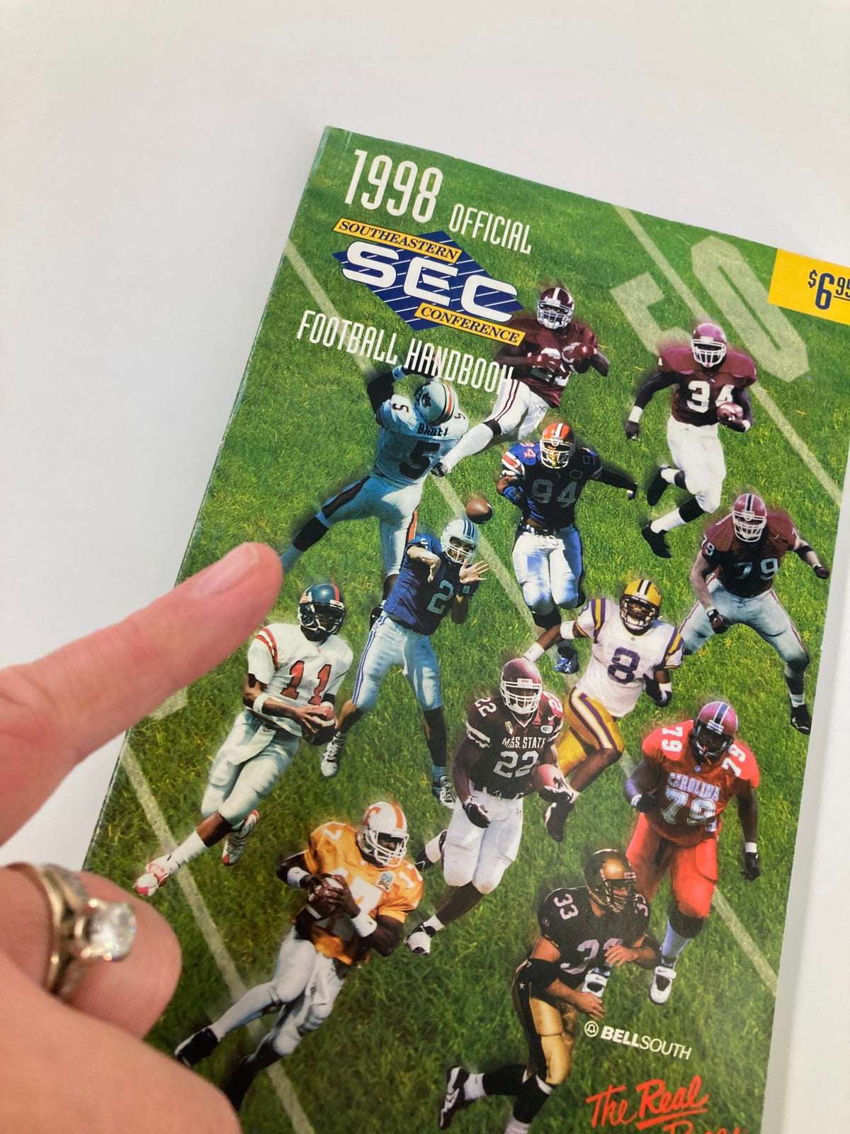 1998 Official Southeastern Conference Football Handbook cover with a hand pointing, showing highlights of football players in action.