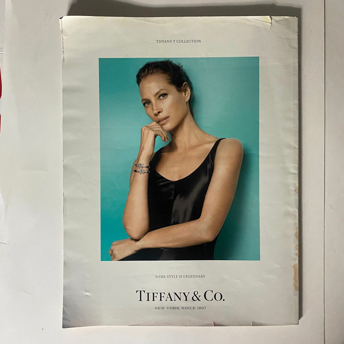 Advertisement from Tiffany & Co. featuring a model in elegant attire, promoting the Tiffany Collection, with a striking teal background.