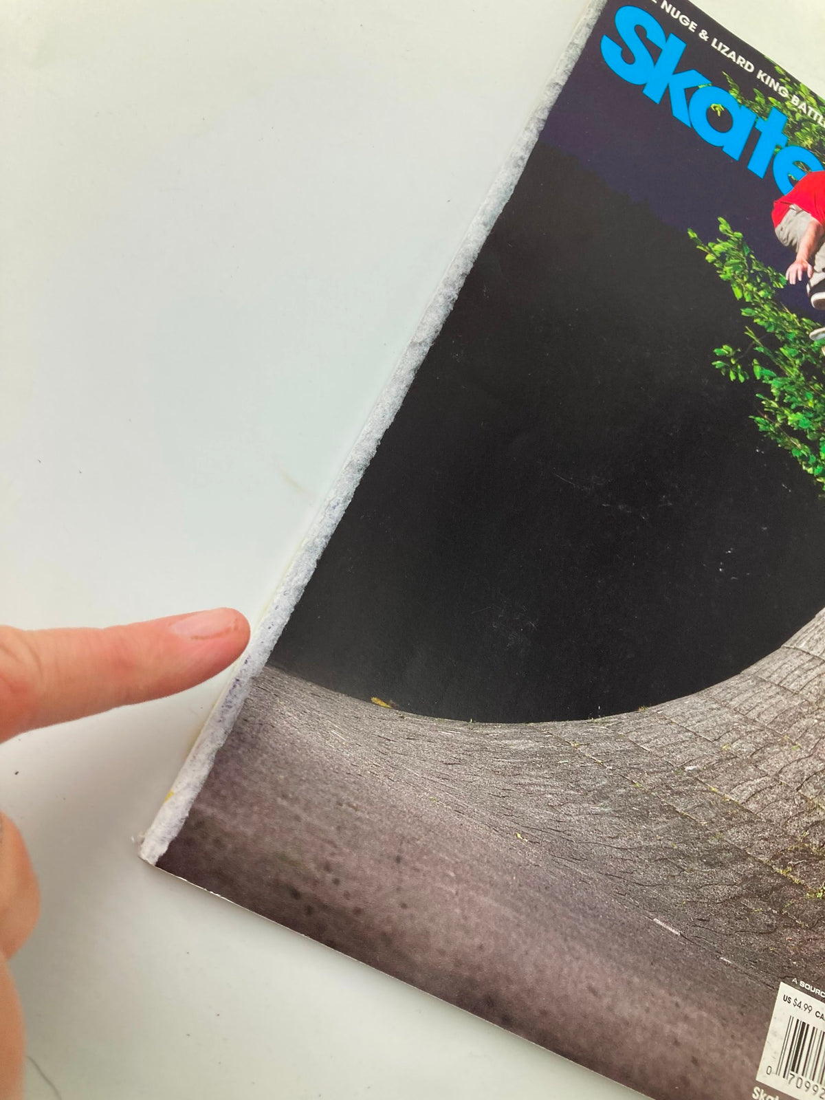 Detail of the spine of Skateboarder Magazine July 2009 Vol 18 #11 showing minor wear typical of its age, with a hand pointing at the edge.