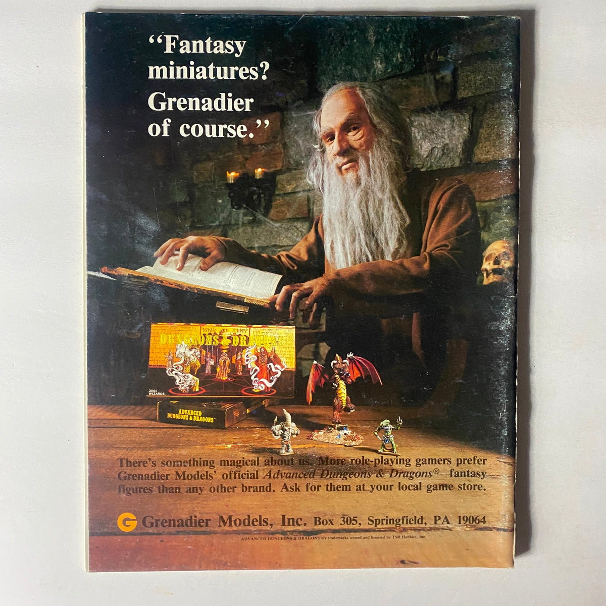 Back cover of Dragon Magazine January 1982, Issue #57 featuring an advertisement for Grenadier Models with a wizard reviewing fantasy miniatures for Dungeons & Dragons.