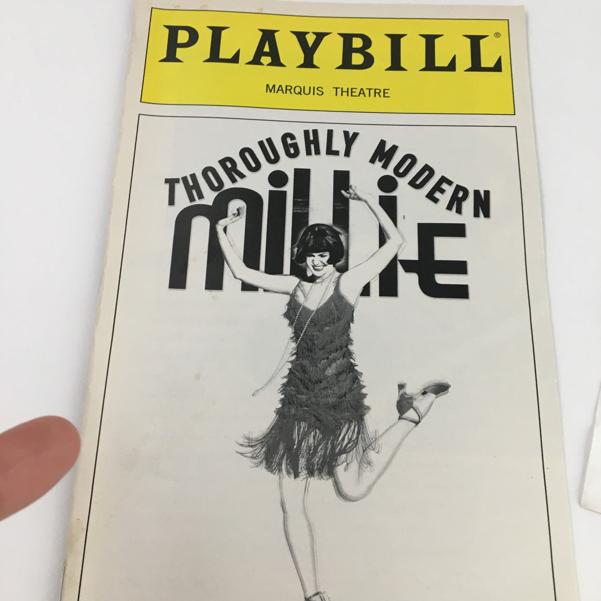 Close-up of the 2002 Thoroughly Modern Millie Playbill cover, highlighting the striking title design and the character's joyful pose, symbolizing the vibrant spirit of the musical.