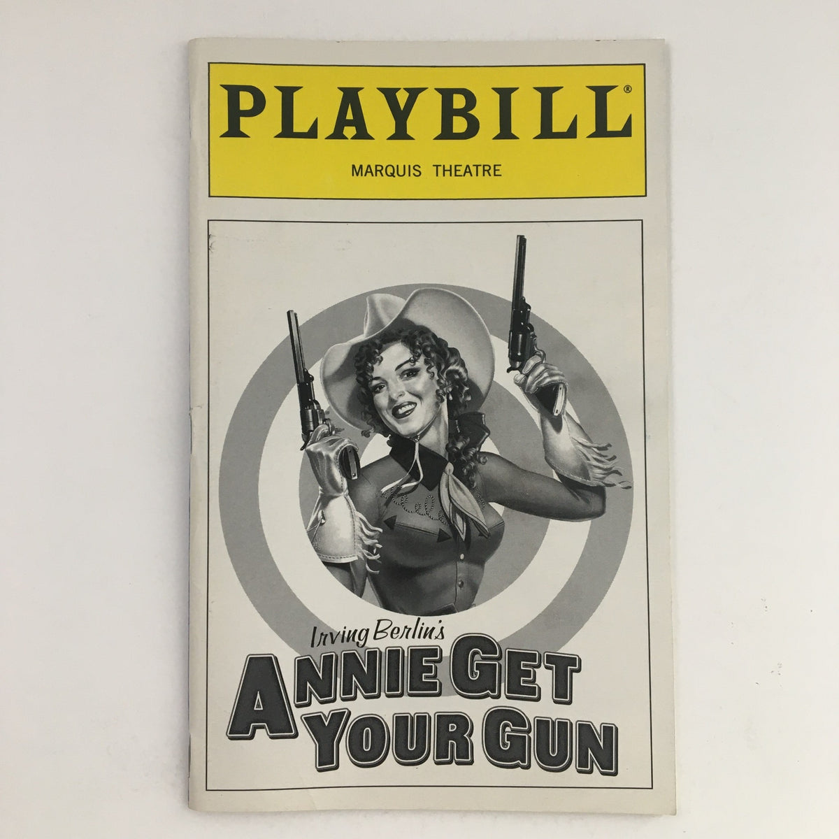 1999 Playbill for Annie Get Your Gun at Marquis Theatre featuring an iconic image of a performer holding two guns, representing the classic Broadway musical.