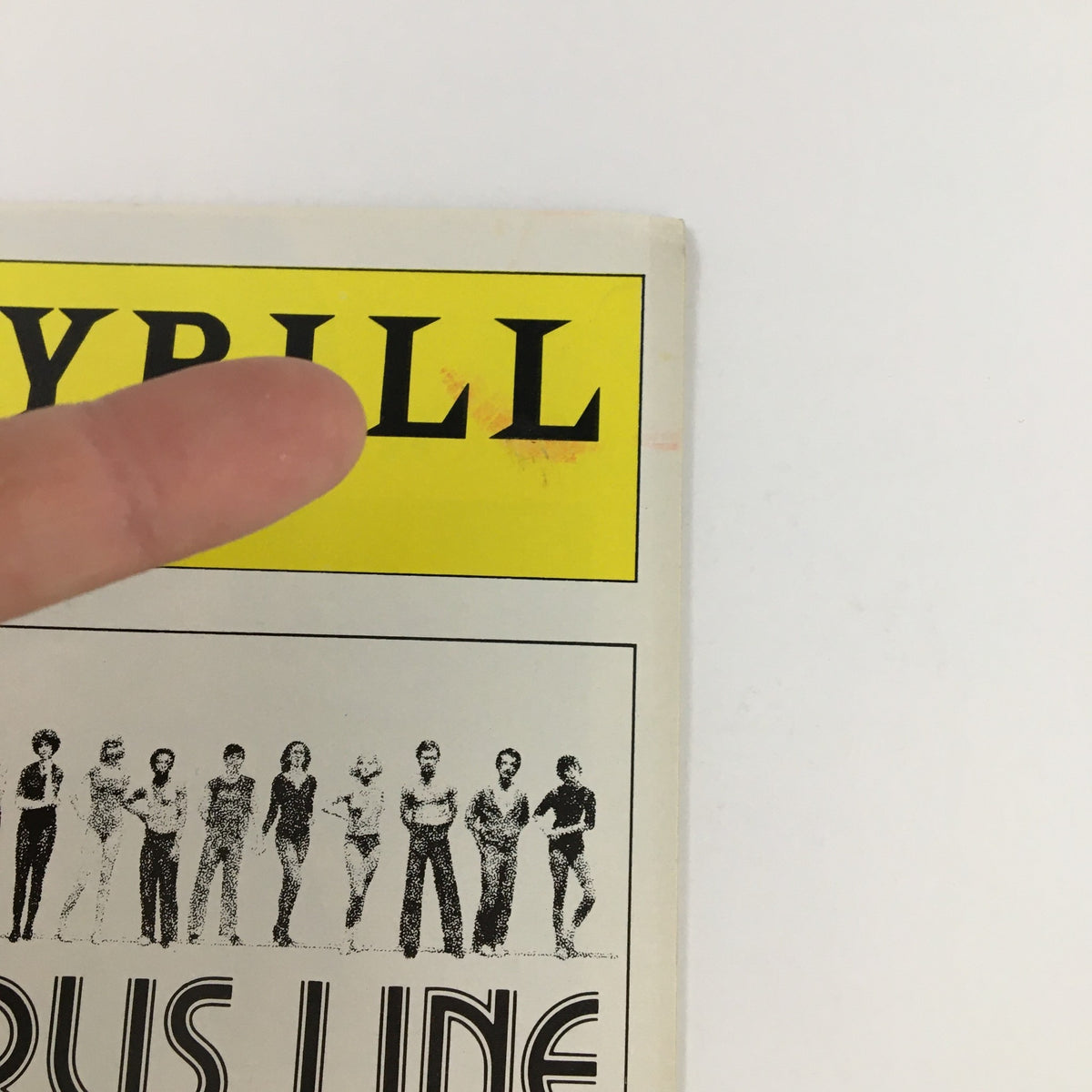 Close-up of the 1977 Playbill for A Chorus Line by Michael Bennett, highlighting the title logo and a finger pointing at it.