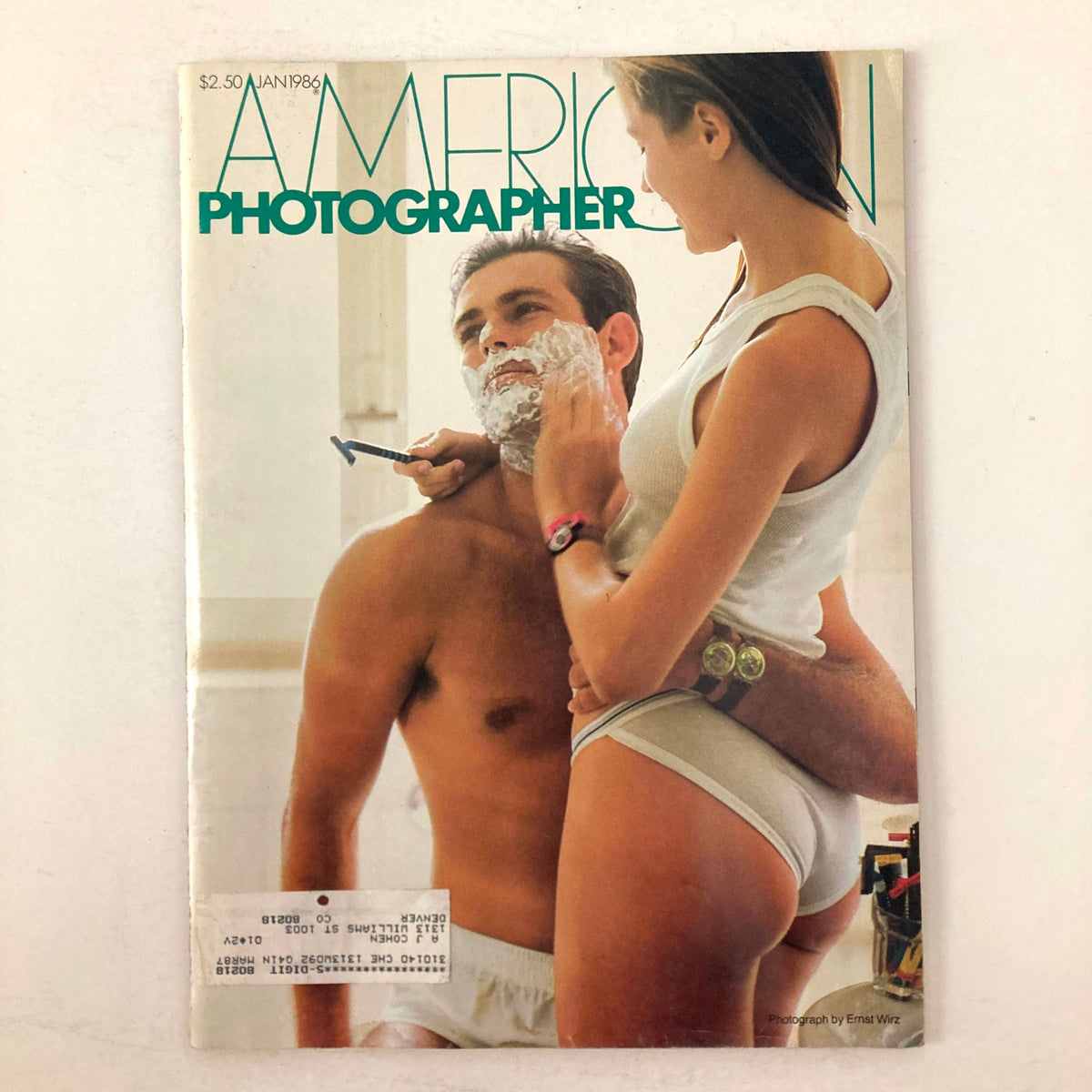 Cover of American Photographer Magazine January 1986 featuring a man receiving a shave while a woman in casual attire interacts closely, showcasing the magazine's theme 'Close Shave for Swatch Company'.