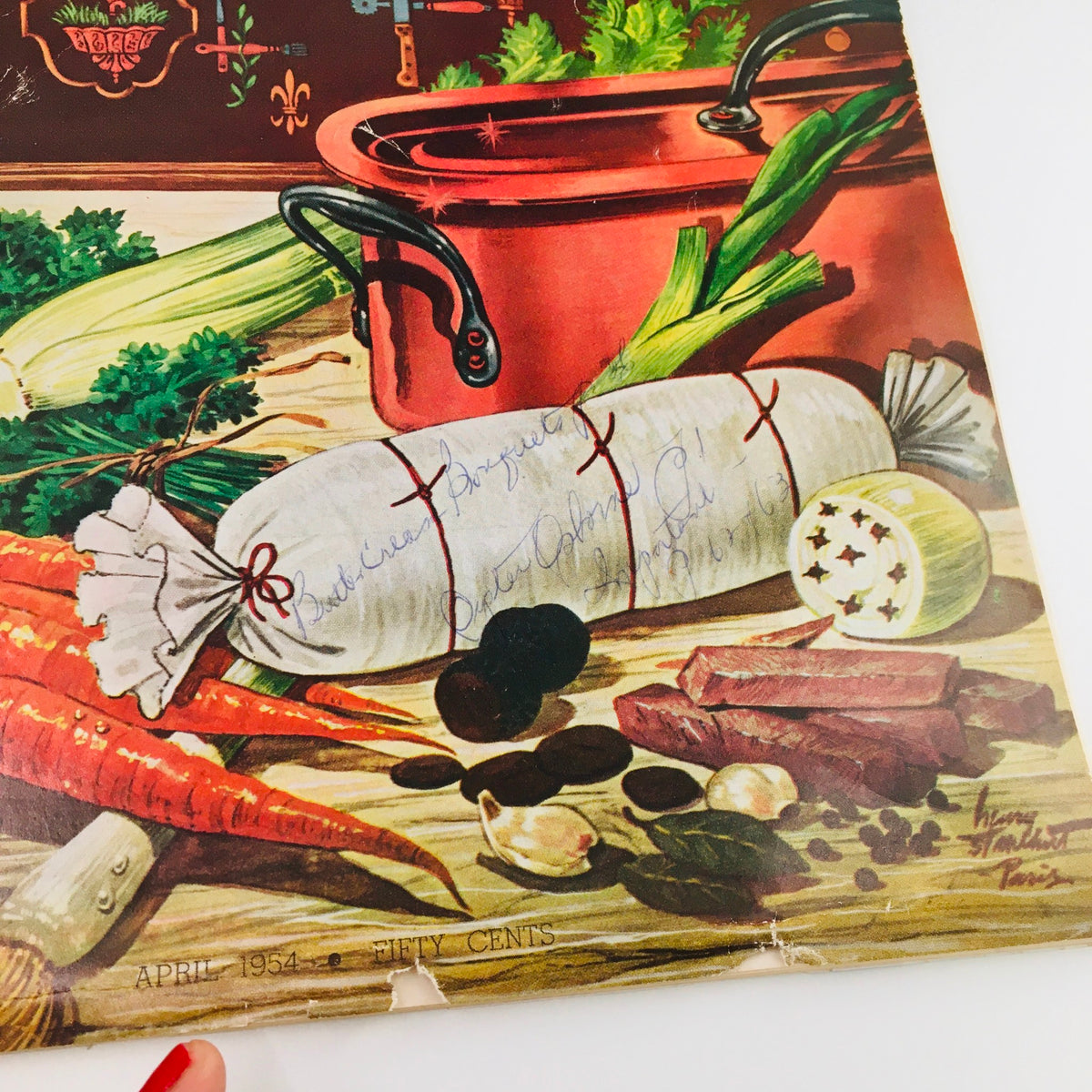 Close-up detail of the cover of Gourmet Magazine April 1954, showcasing an artistic rendering of a white rolled dish with handwritten notes, surrounded by colorful vegetables and a pot, emphasizing its vintage culinary charm.