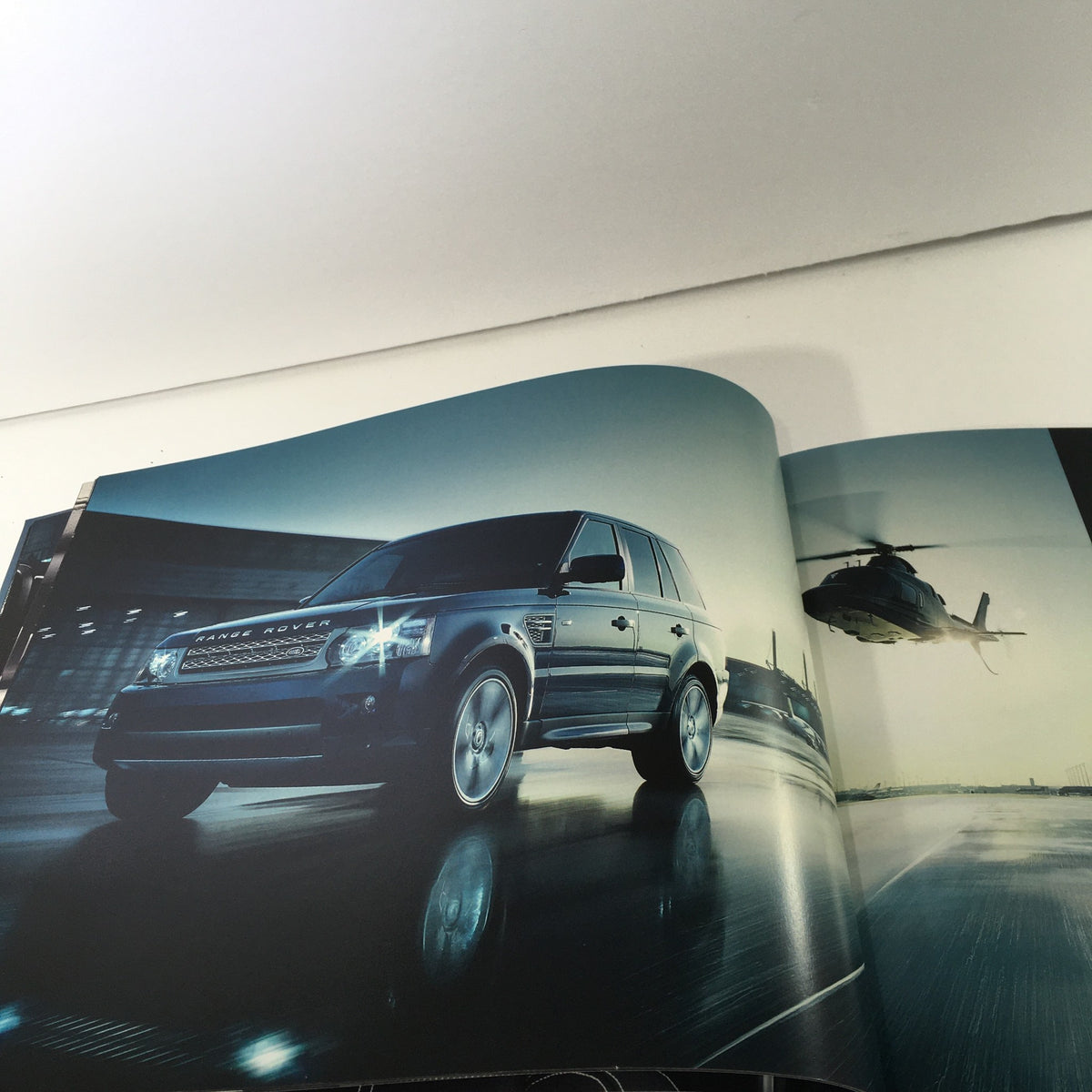 Exterior shot of the 2010 Land Rover Range Rover Sport Dealership Car Auto Brochure Catalog, featuring the vehicle near a helicopter in a dynamic setting.
