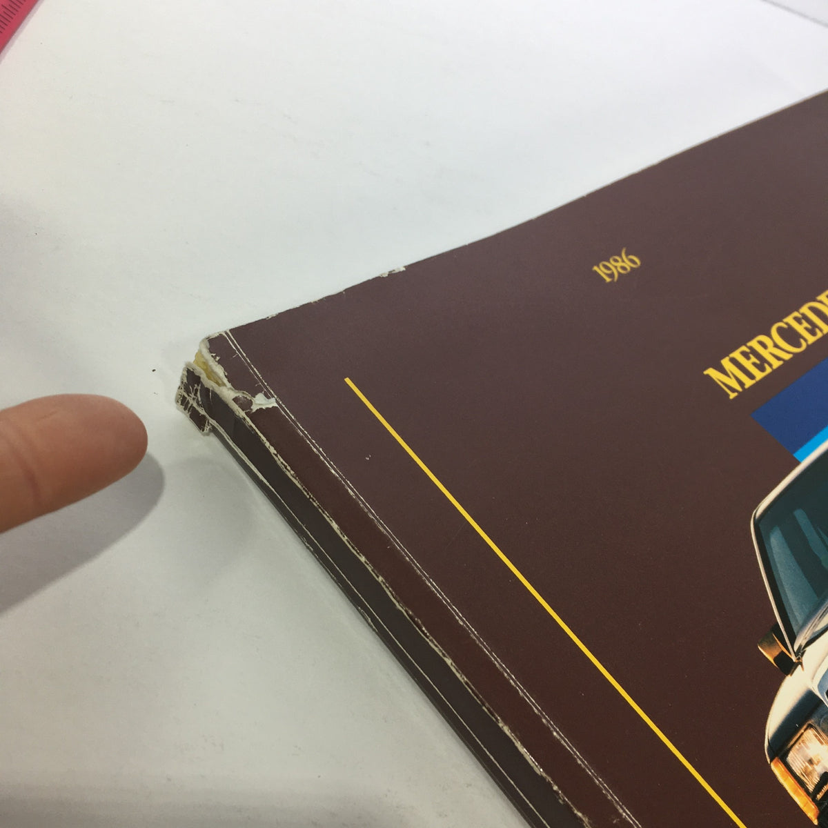 Damage detail on the spine of the 1986 Mercedes-Benz Product and Sales Information Brochure showing wear and tear.
