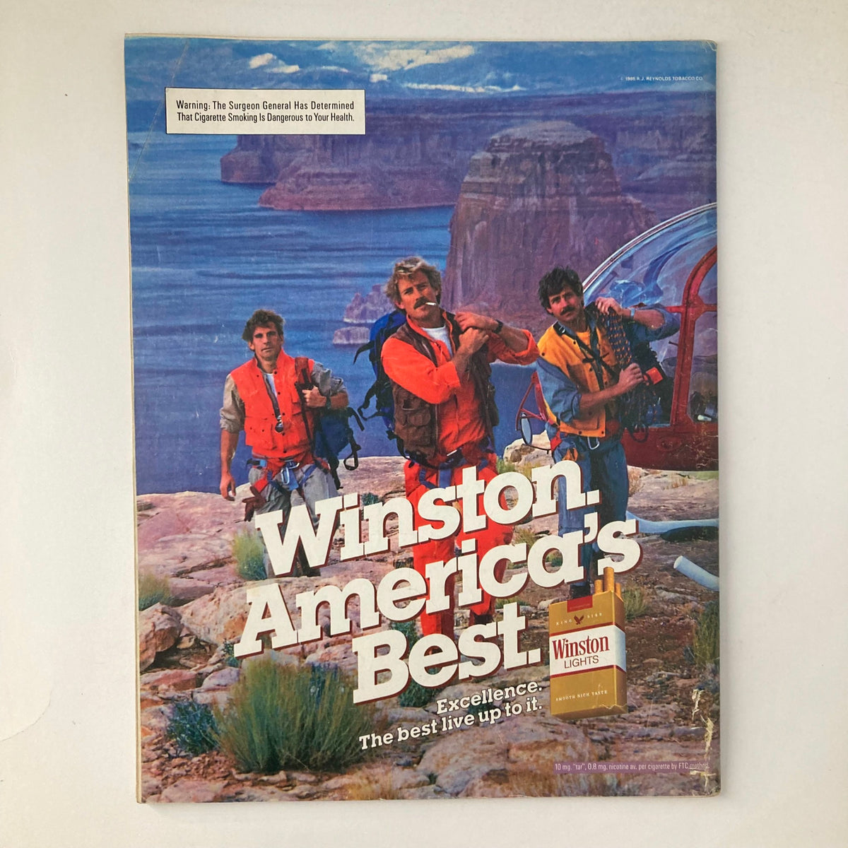Cover of Winston, America's Best cigarette advertisement featuring three men in outdoor gear against a scenic background, promoting excellence with Winston Lights branding.