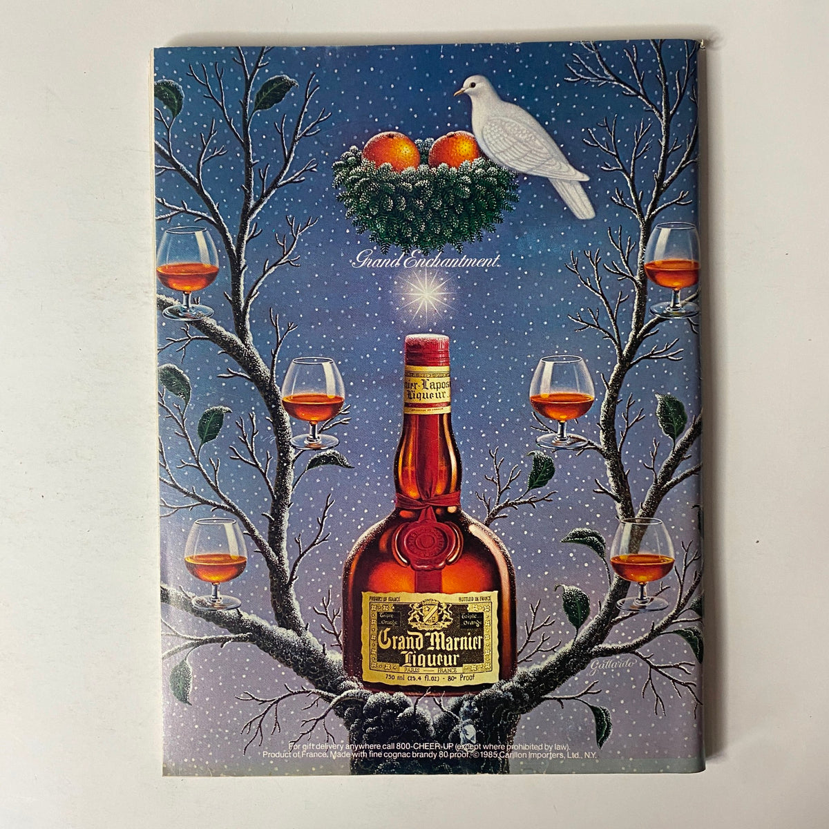 Artistic advertisement for Grand Marnier liqueur featuring a bottle amidst winter scenery with glasses of liqueur on branches, titled 'Forbes Magazine December 16, 1985 Spendthrift America? The Myth Exposed'.