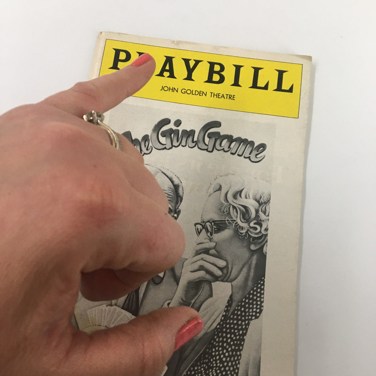A close-up of the 1978 Playbill for The Gin Game by D.L. Coburn, with a hand pointing at the cover that highlights the title and illustrations, from the John Golden Theatre.