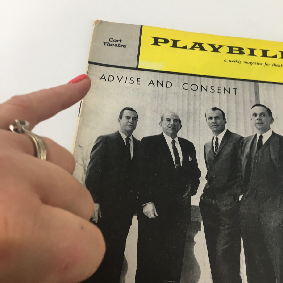 Close-up of the 1960 Playbill for Advise and Consent at Cort Theatre, showing a hand pointing to the title on the cover.