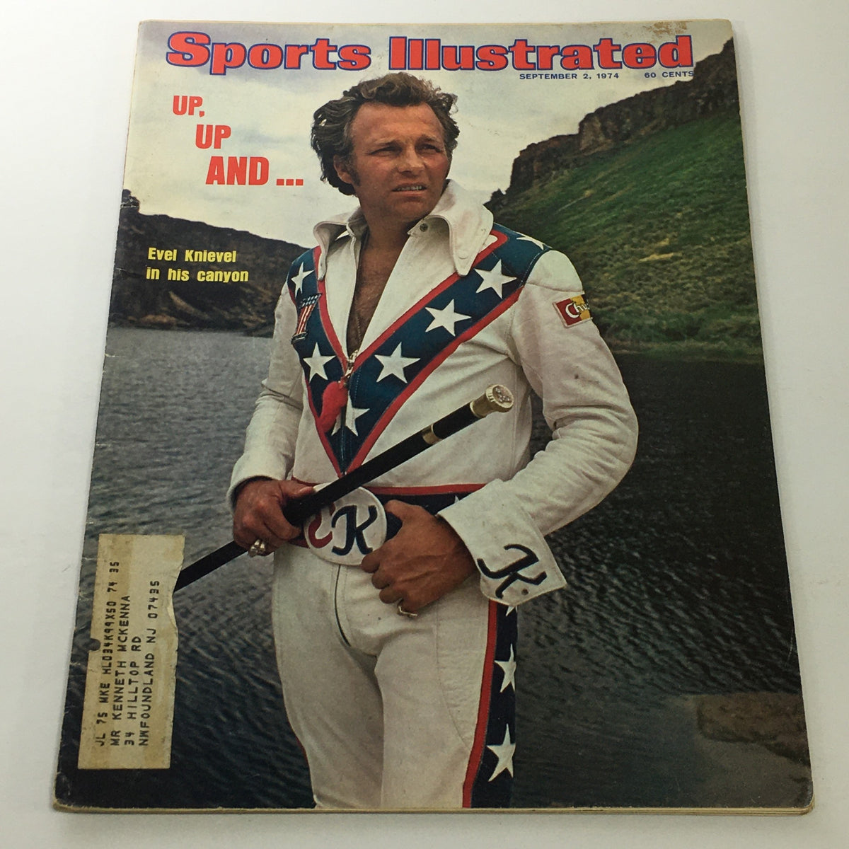 Cover of Sports Illustrated magazine from September 2, 1974, featuring Evel Knievel in his canyon, wearing a patriotic outfit with stars and stripes, holding a cane, and standing against a backdrop of rocky terrain and water.