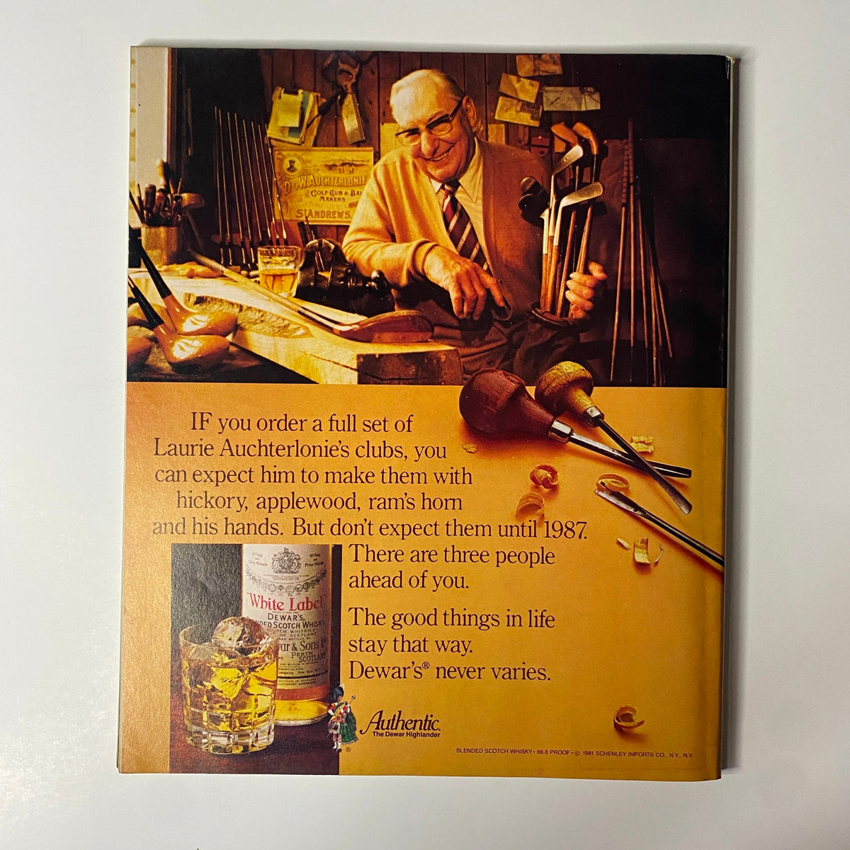 An advertisement featuring a smiling elder man in a workshop, surrounded by woodworking tools. The ad promotes Laurie Auchterlonie's golf clubs made from various materials, paired with a Dewar's whiskey drink. Includes elements about waiting times for club orders, emphasizing quality and craftsmanship. Related to the Fortune Magazine September 21, 1981 issue highlighting Ronald Reagan’s First 200 Days.