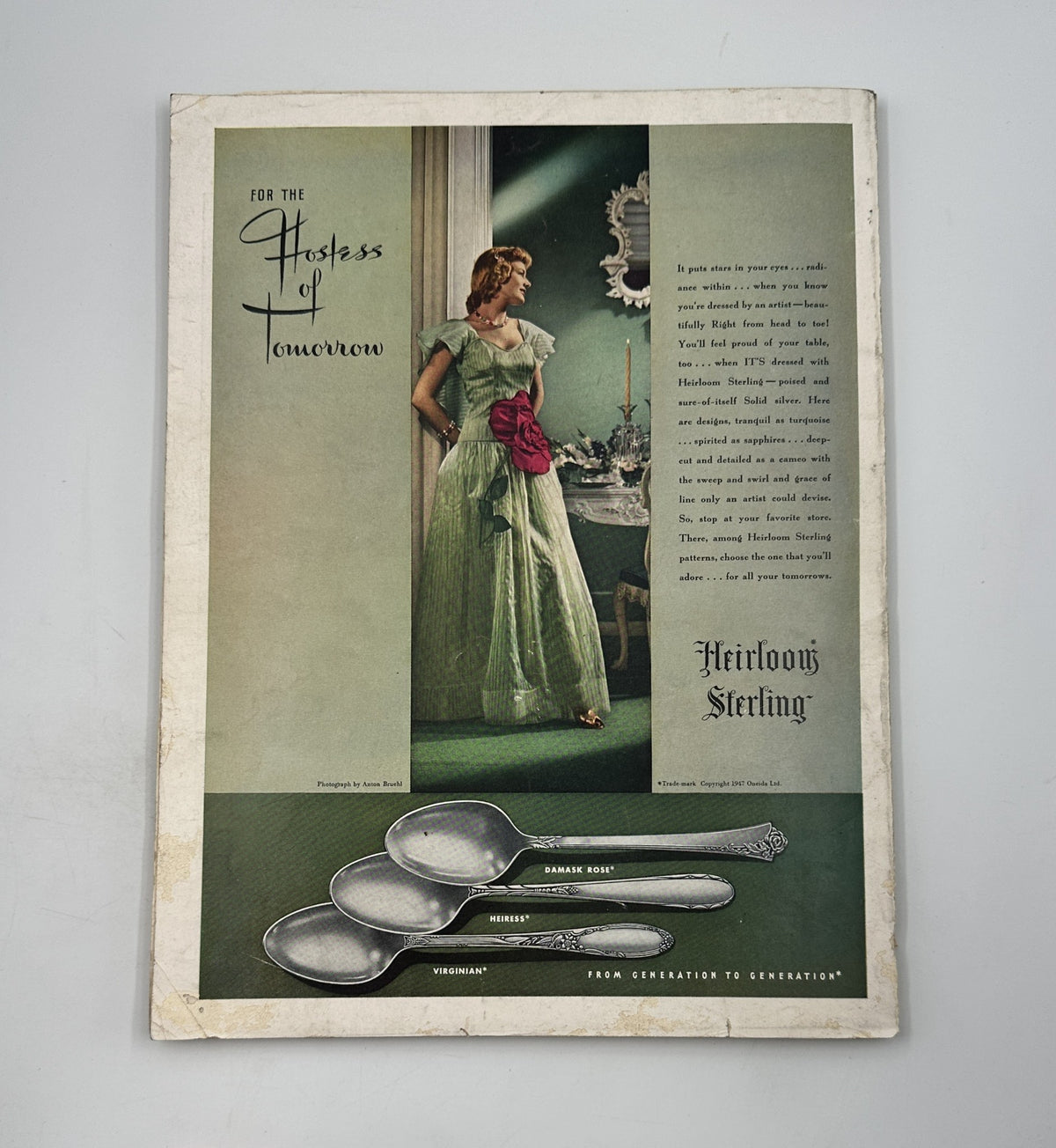 A sophisticated advertisement from House Beautiful Magazine September 1947, featuring an elegant woman in a vintage gown with silverware, emphasizing style and hospitality.