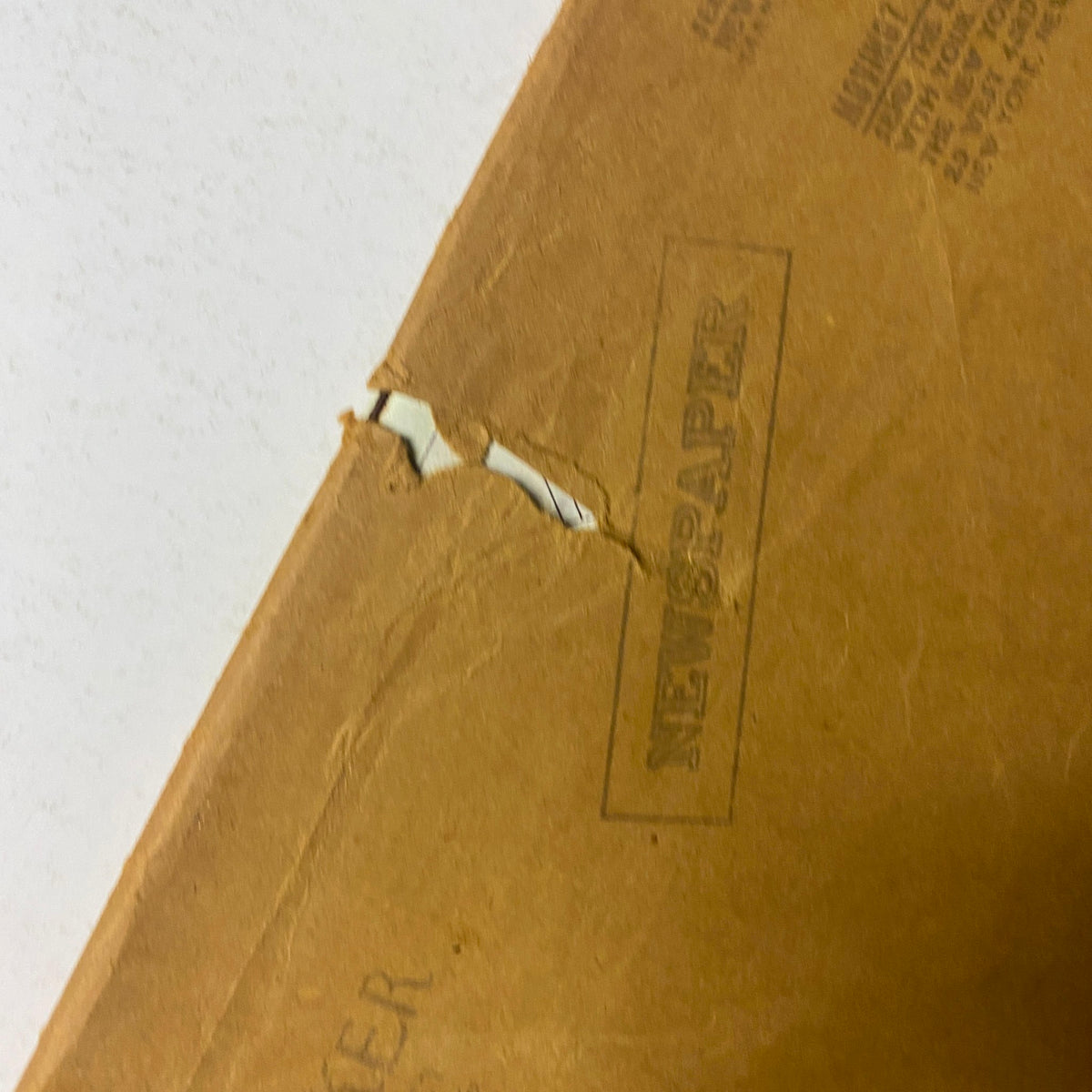 Close-up view of the back cover of The New Yorker magazine, June 14, 1976, highlighting a tear in the packaging and the printed word "NEWSPAPER" on the vintage brown paper.