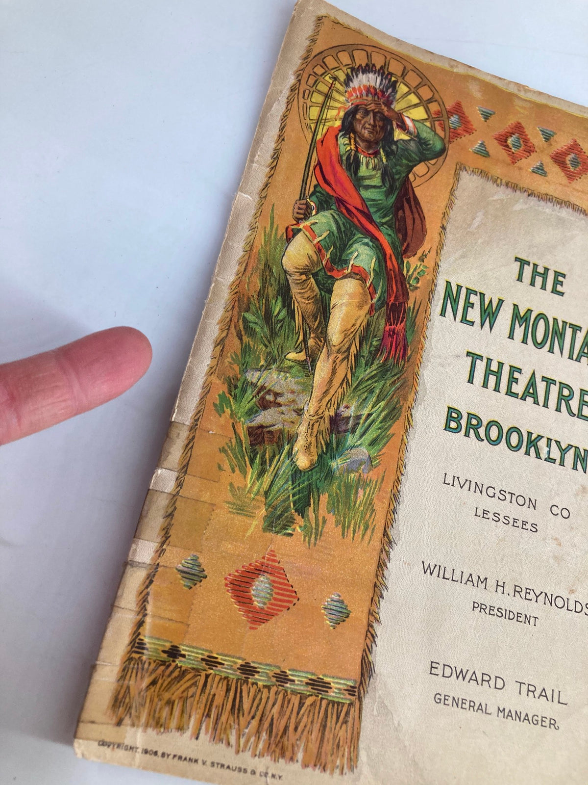 Close-up of the cover of the 1913 The New Montauk Theatre Brooklyn Playbill, highlighting the intricate details of the illustration and the title, with a finger pointing to enhance perspective.