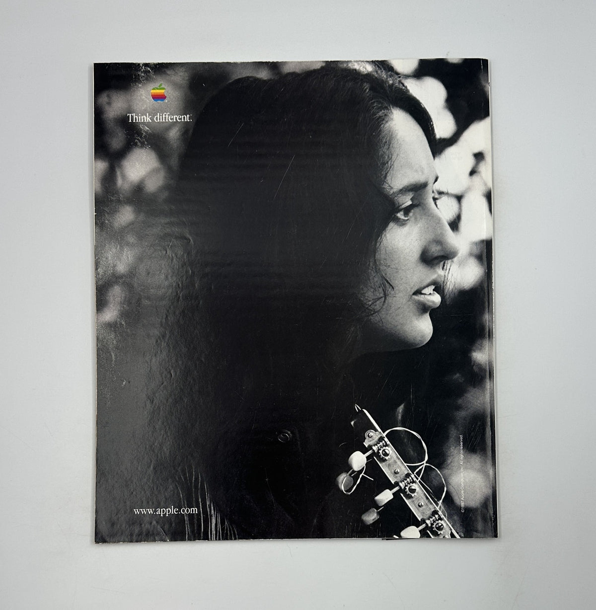 Back cover of George Magazine January 1998 featuring a vintage advertisement by Apple with the slogan 'Think different,' complemented by a black-and-white image of a woman playing a guitar.