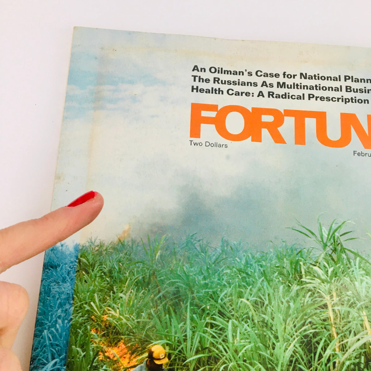 Close-up of the Fortune Magazine February 1977 cover with the title 'Sugar After The Boom and Bust'. A finger points to the magazine, emphasizing the agricultural scene of sugar cane in the background.