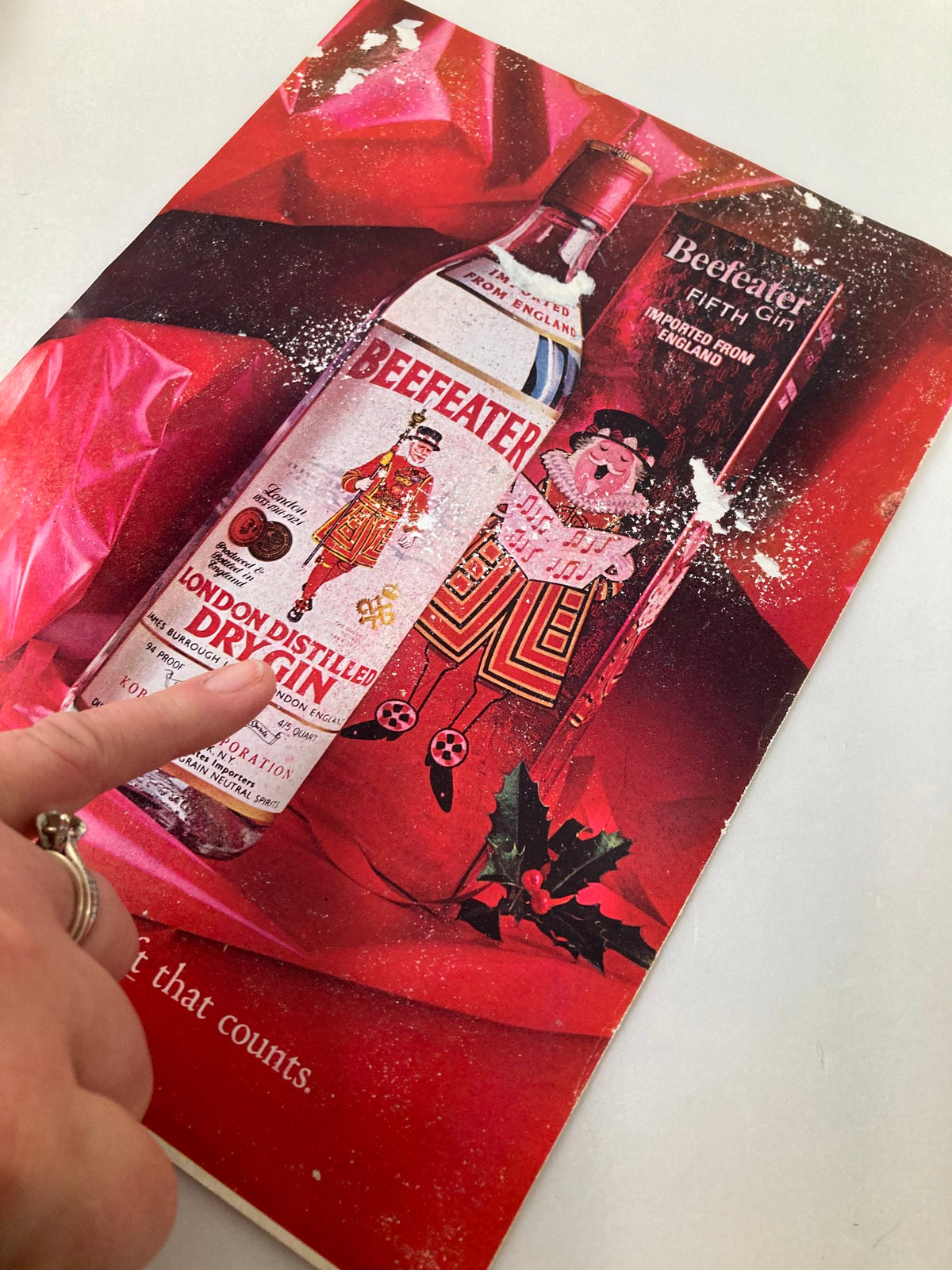 Vintage advertisement featuring Beefeater London Distilled Dry Gin, highlighted on a festive red background with holly, adding a nostalgic touch.