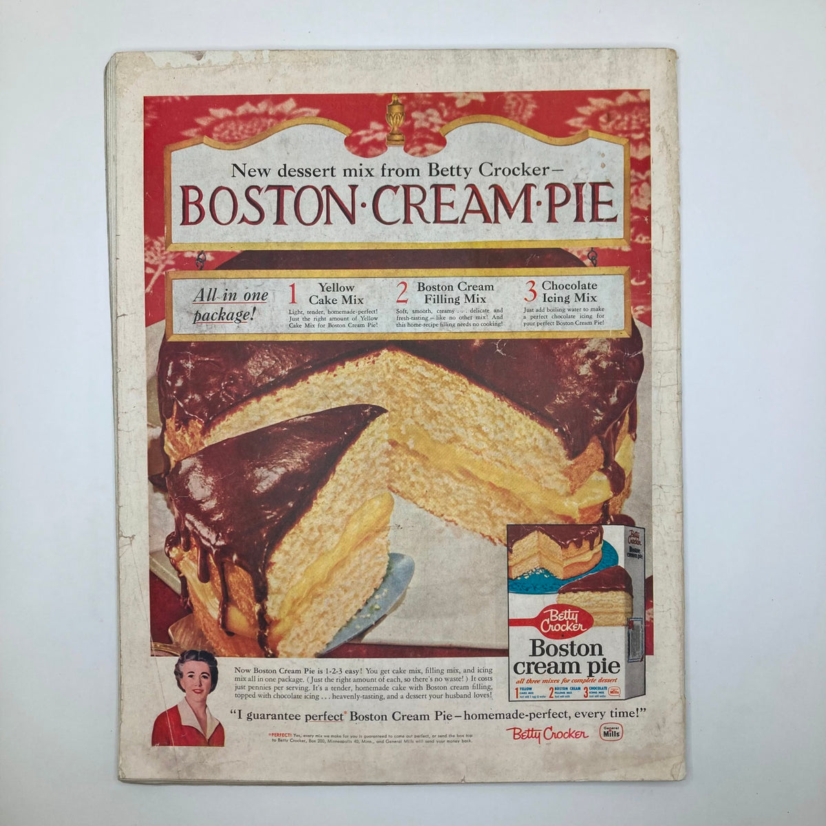 Cover of the Boston Cream Pie dessert mix from Betty Crocker, showcasing the cake with chocolate icing and filling. This vintage packaging emphasizes the ease of use with an all-in-one package for creating homemade desserts.