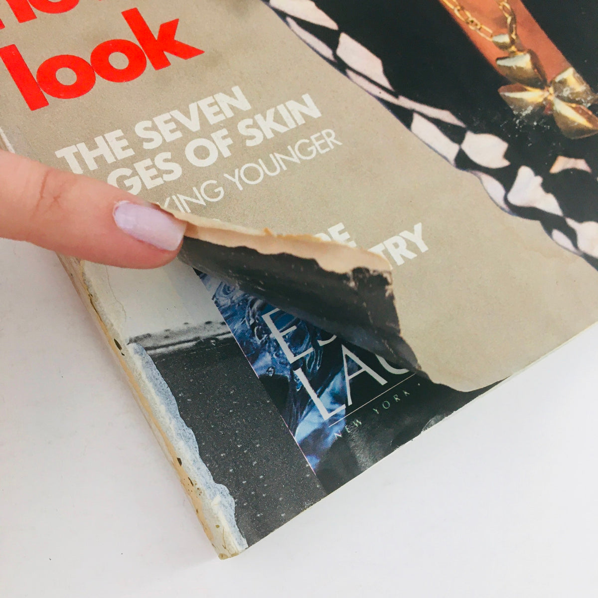 Close-up of Vogue Magazine January 1990 with a finger pointing at a peeling corner, revealing details of the magazine's vintage condition and cover text.