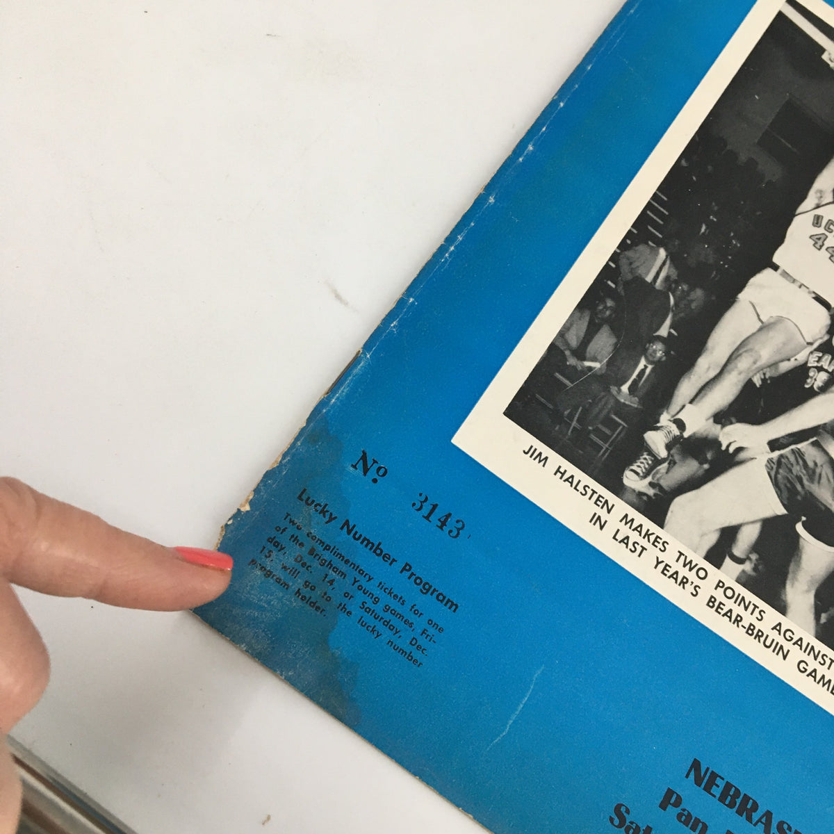 Close-up of the corner of the official program from December 1, 1956 NCAA Basketball game Nebraska vs UCLA. Highlights the 'Lucky Number Program' note and the minor wear on the edges.