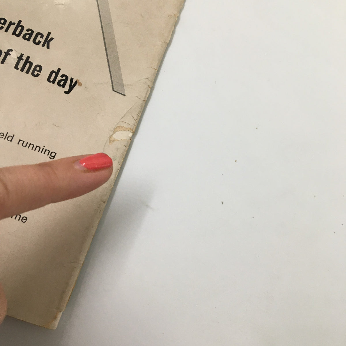 Detail of a worn corner on the September 20 1963 NCAA Football Pitt vs UCLA The Goal Post Official Program with a finger pointing to the damage.