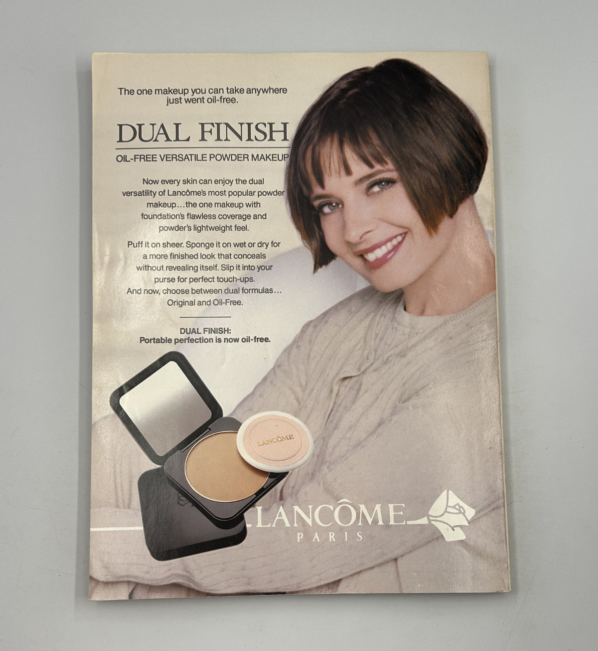 Advertisement for Lancôme Paris featuring a model with a chic bob hairstyle promoting Dual Finish oil-free versatile powder makeup, included within the Vanity Fair Magazine October 1994.