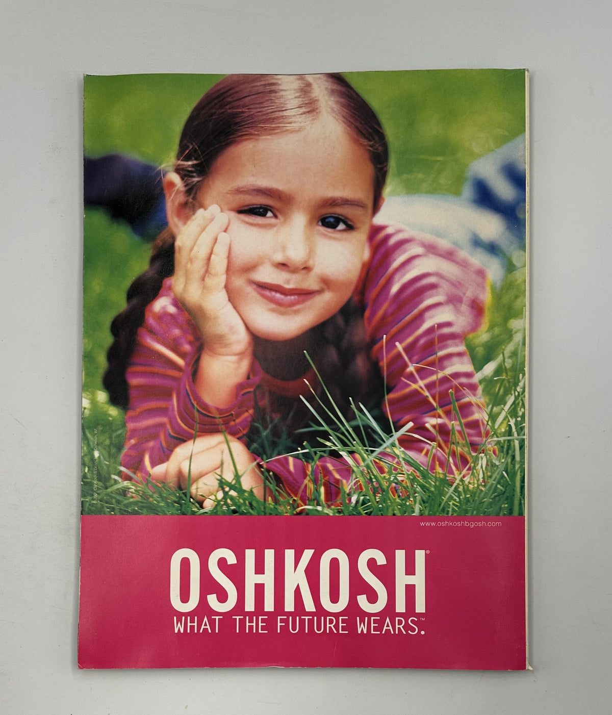 OshKosh advertisement from a magazine featuring a young girl in a grassy field, promoting children's fashion with the slogan 'WHAT THE FUTURE WEARS'.