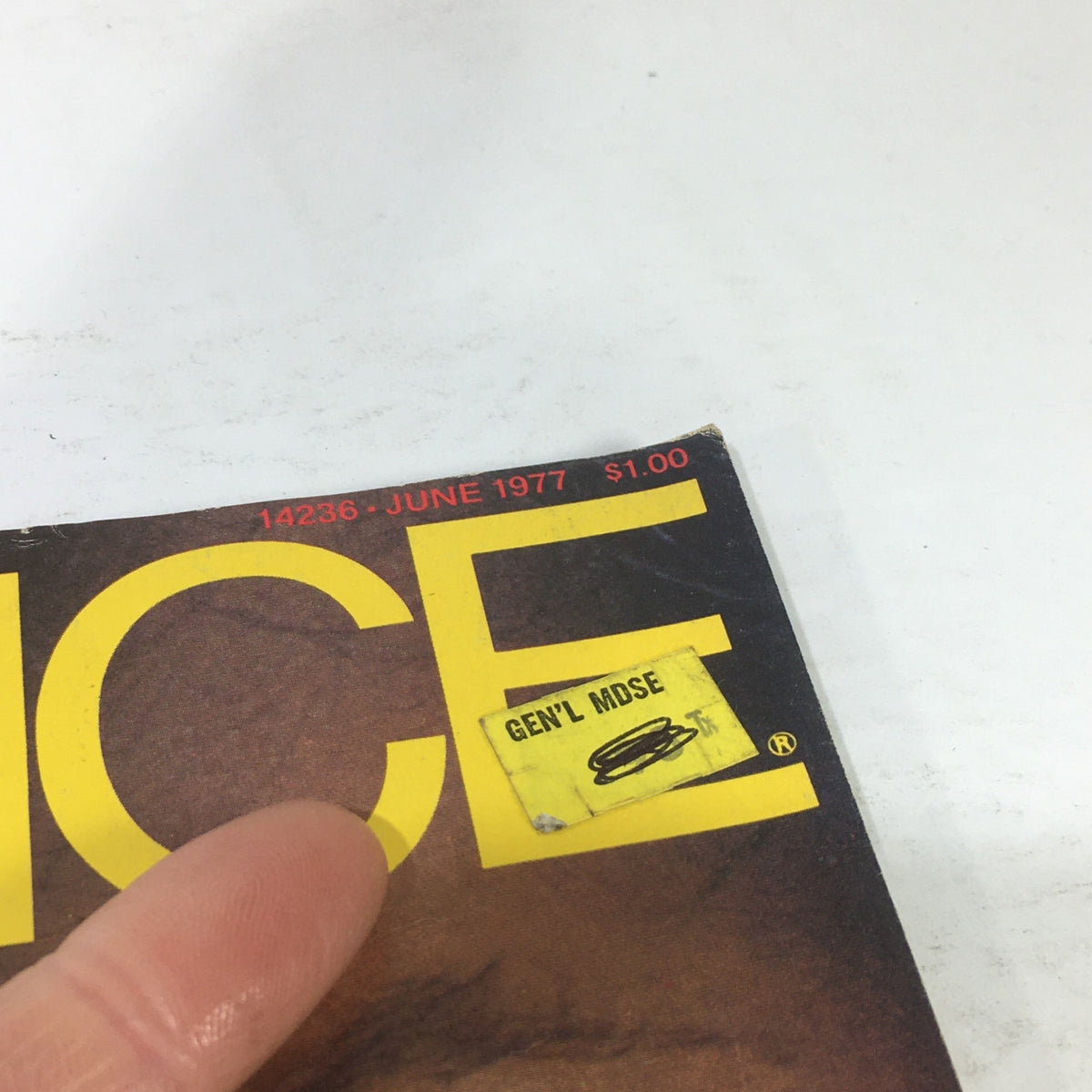 Close-up view of the June 1977 Essence Magazine with Louis Gossett cover, showing labeled price sticker and finger pointing, emphasizing the vintage aspect of this collectible magazine.