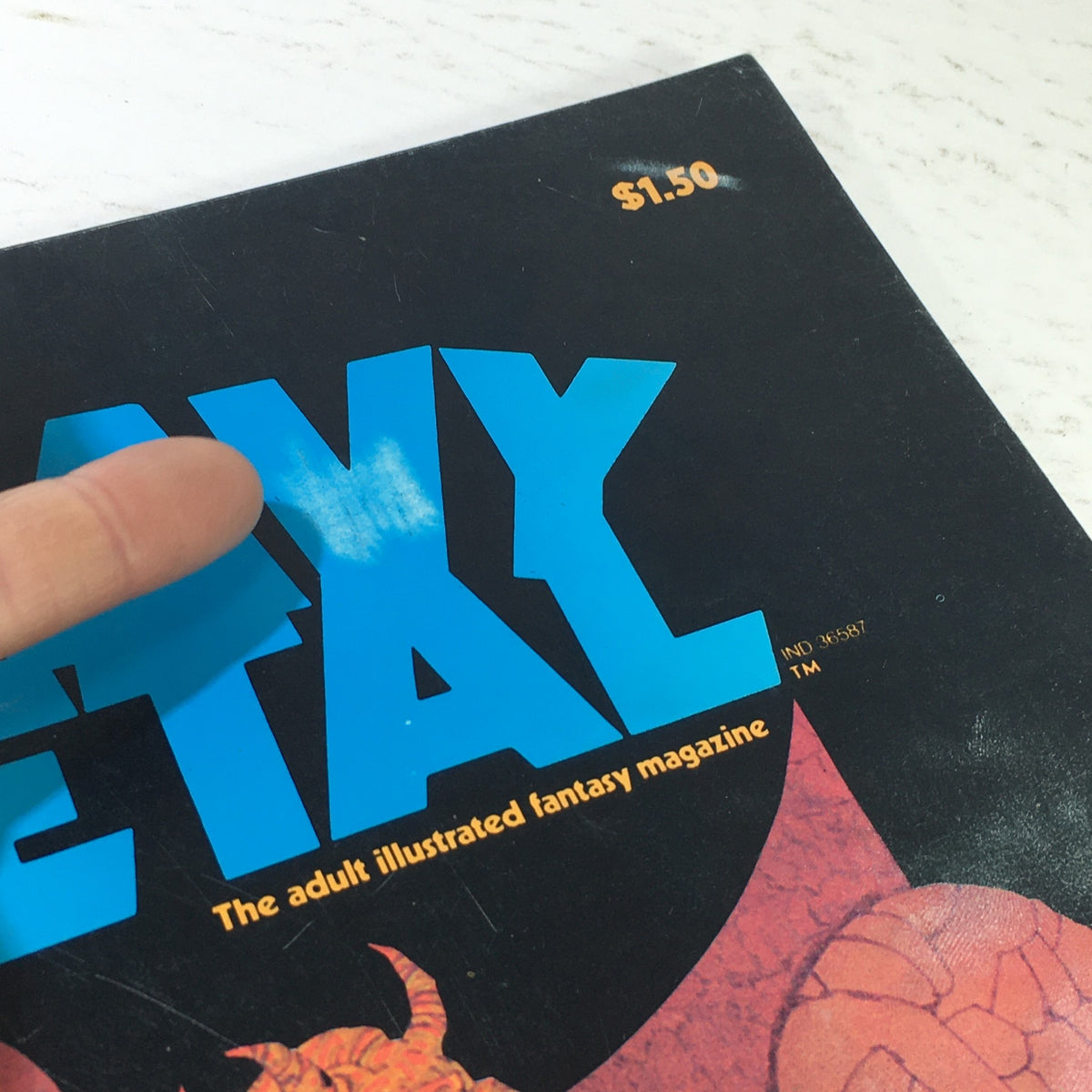 Close-up of the prominent title on the cover of VTG Heavy Metal Magazine: February 1978 with a finger pointing, emphasizing its bold typography and unique artwork.