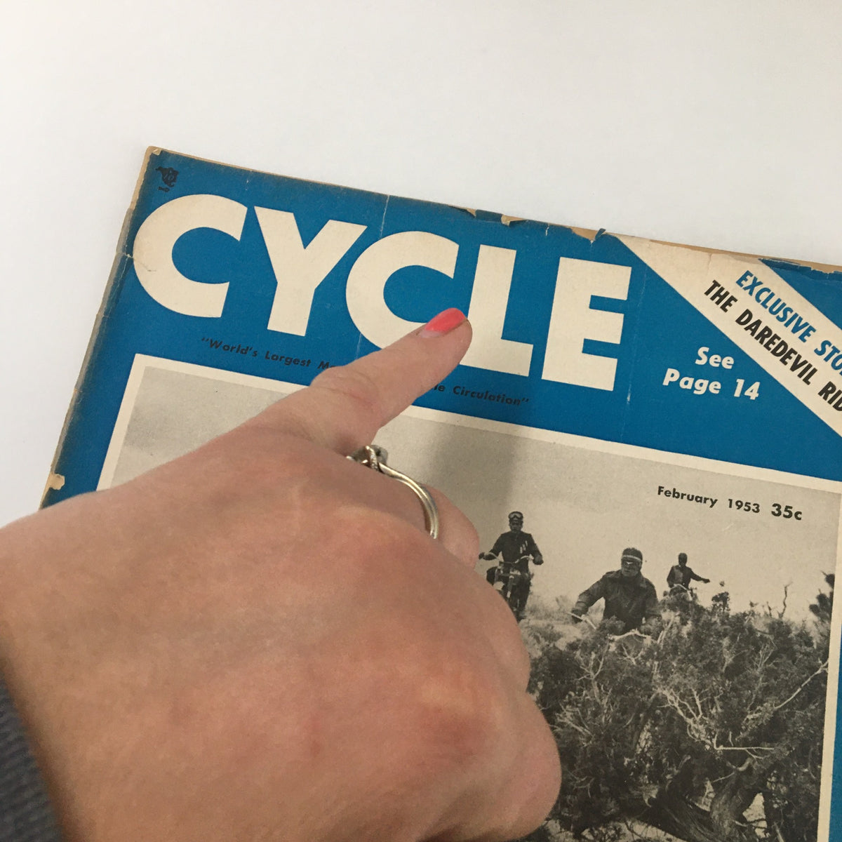 Close-up of the cover of VTG Cycle Magazine February 1953 highlighting the title 'CYCLE' and an exclusive story 'The Daredevil Rider' with a hand pointing to the title.