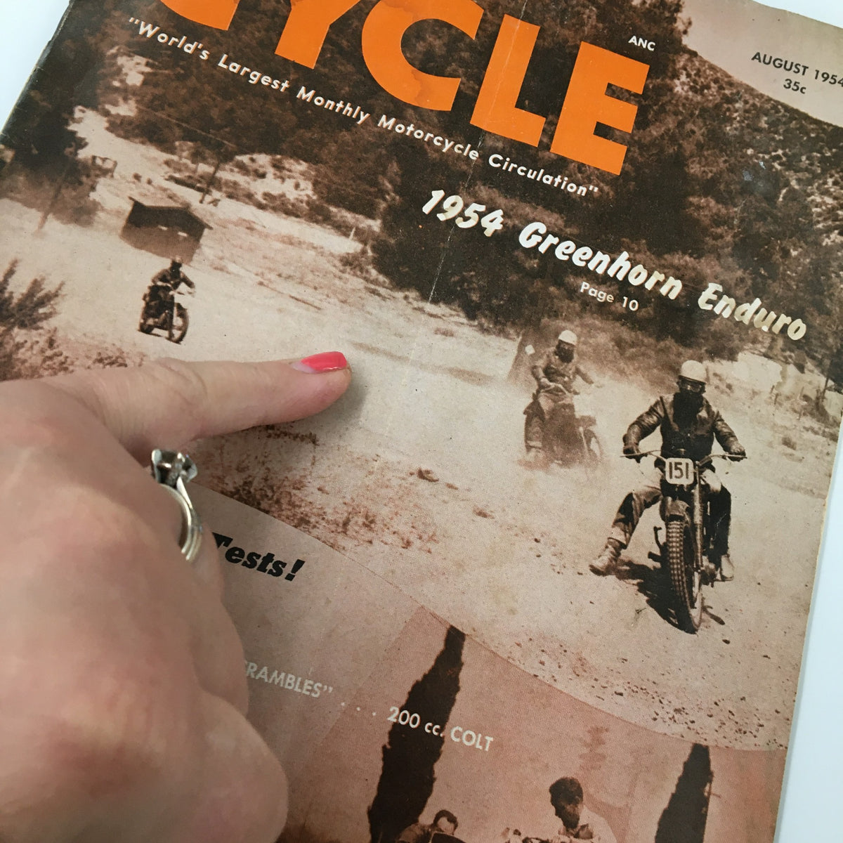 Close-up view of the VTG Cycle Magazine August 1954 cover, highlighting the Greenhorn Enduro event and featuring a hand pointing at an image.