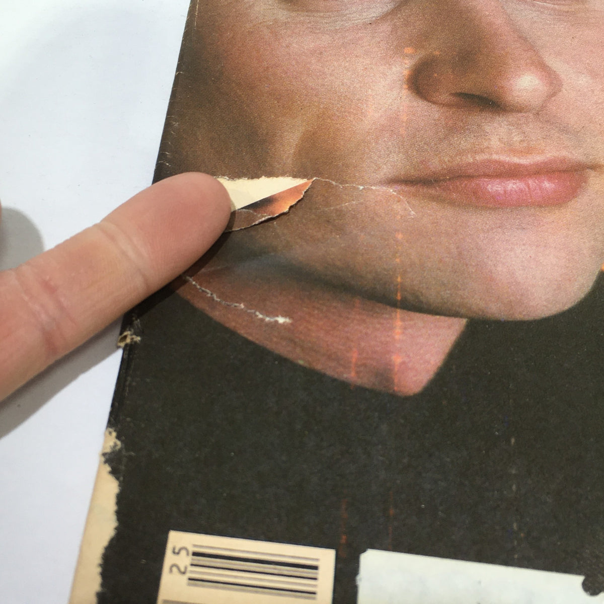 Close-up of a damaged section on the back cover of a Vintage Rolling Stone magazine featuring Men At Work, showing a tear and finger pointing at the wear.