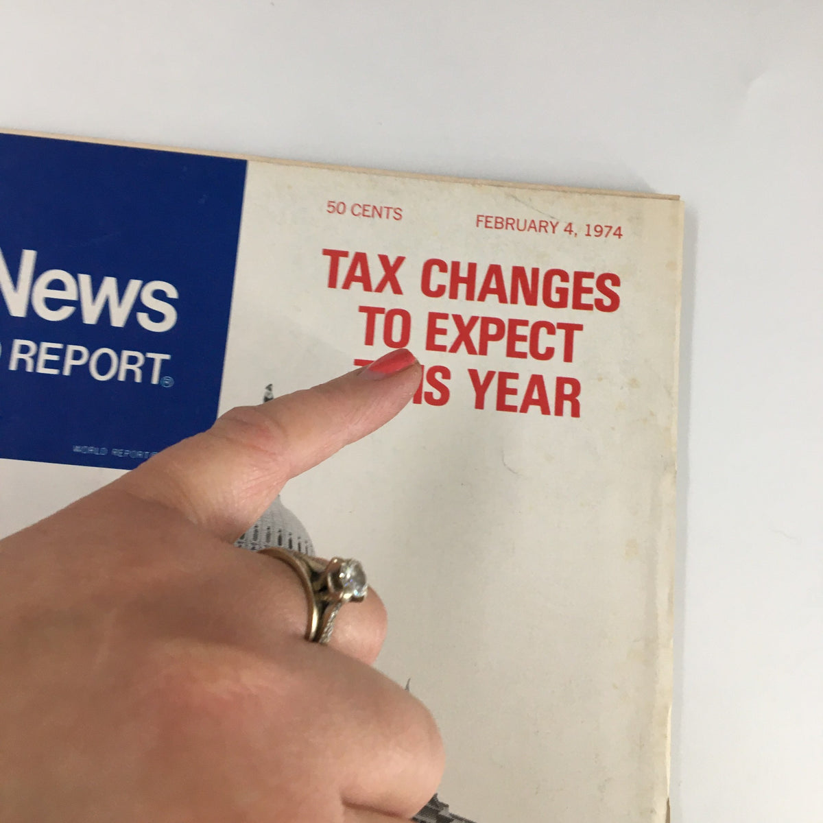 Close-up of the cover of US News & World Report Magazine February 4, 1974, highlighting the title 'Tax Changes to Expect This Year' with a hand pointing to it.