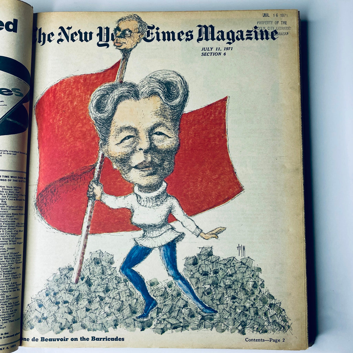 Cover page of The New York Times Magazine, July 11, 1971, showcasing a caricature of Simone de Beauvoir holding a red flag amid a pile of crushed rocks.