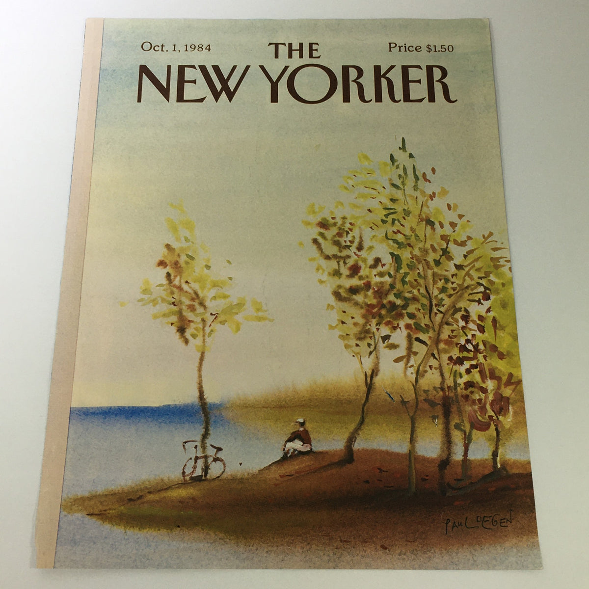 The New Yorker Magazine cover from October 1, 1984, featuring artwork by Paul Degen, depicting a serene landscape with trees, a cyclist, and a person sitting by the water.